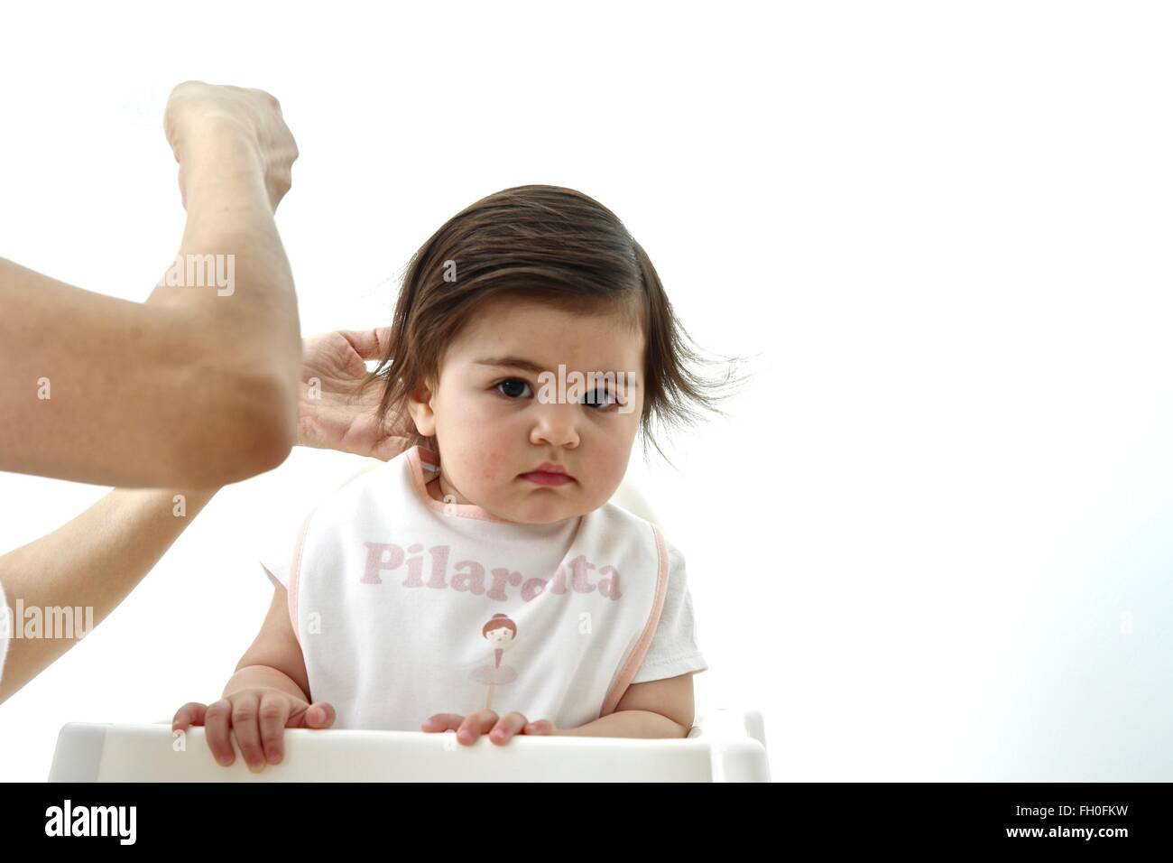 Undici mesi Baby girl curiosamente guardando la telecamera mentre la sua mamma fissa i suoi capelli Foto Stock