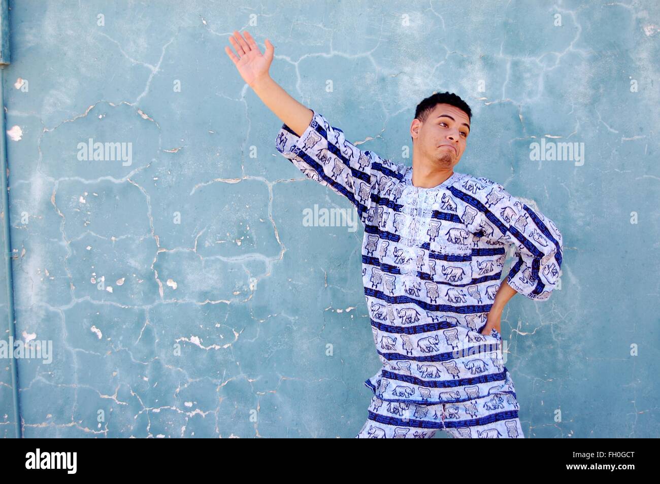 Syrian-Moroccan giovane maschio danze di strada in abito africano di fronte a una frantumazione parete blu downtown Foto Stock