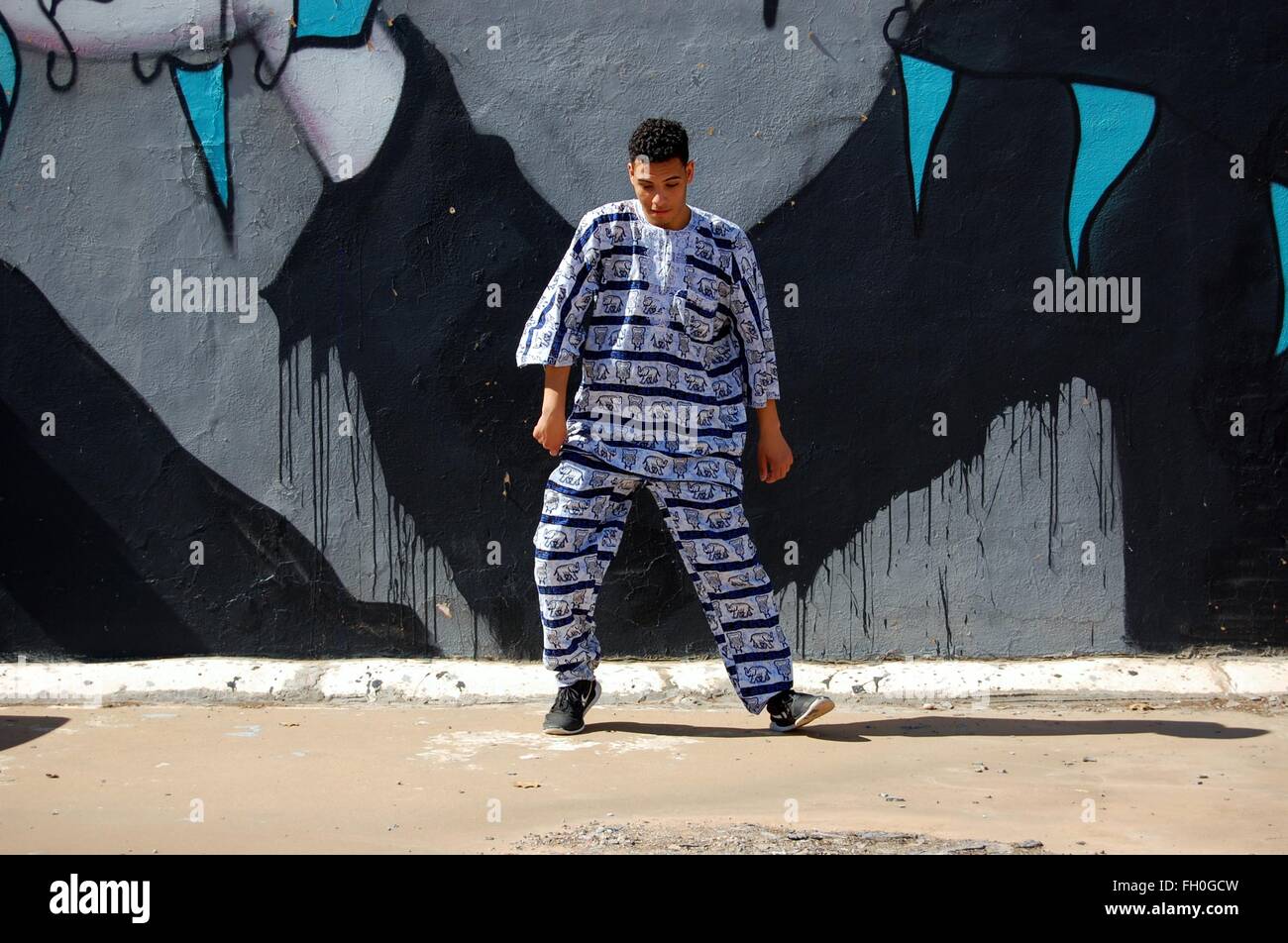 Syrian-Moroccan giovane maschio danze di strada in abito africano nella parte anteriore della parete arte downtown Foto Stock