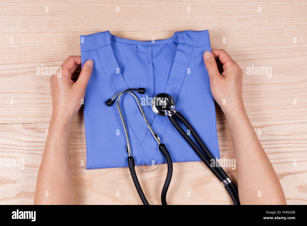 Vista aerea di mani femminili di piegatura scrub medica shirt con uno stetoscopio sulla scrivania in legno. Foto Stock