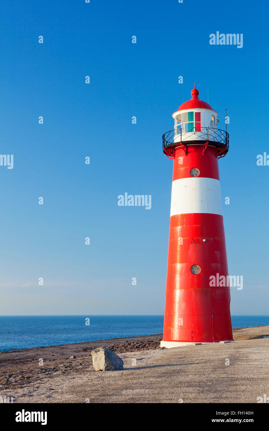 Un rosso e bianco faro di mare sotto un cielo blu chiaro. Fotografato vicino a Westkapelle in Zeeland, Paesi Bassi. Foto Stock