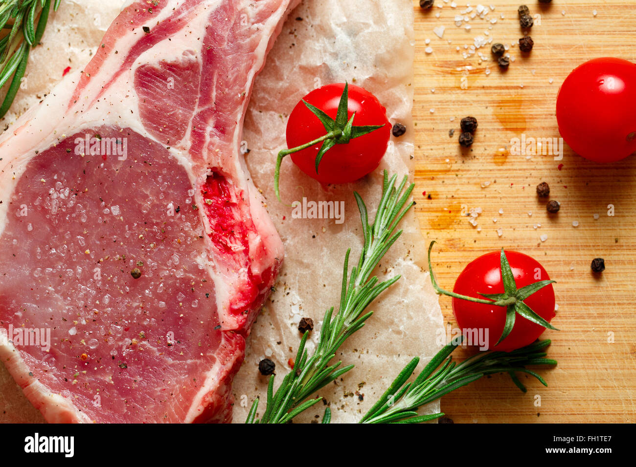 Pezzi di carne cruda con rosmarino e pomodori. Foto Stock