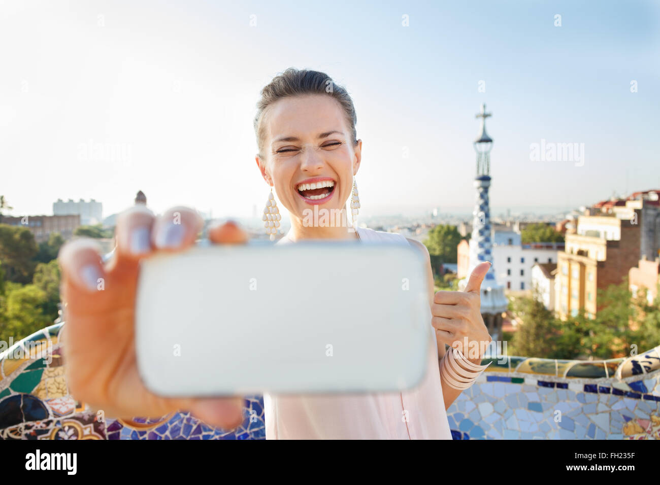 Passeggiata rinfrescante in un unico Parco Guell stile in Barcellona, Spagna. Ritratto di sorridente giovane donna che mostra Thumbs up e tenendo selfie con lo smartphone mentre nel parco Guell, Barcellona, Spagna Foto Stock