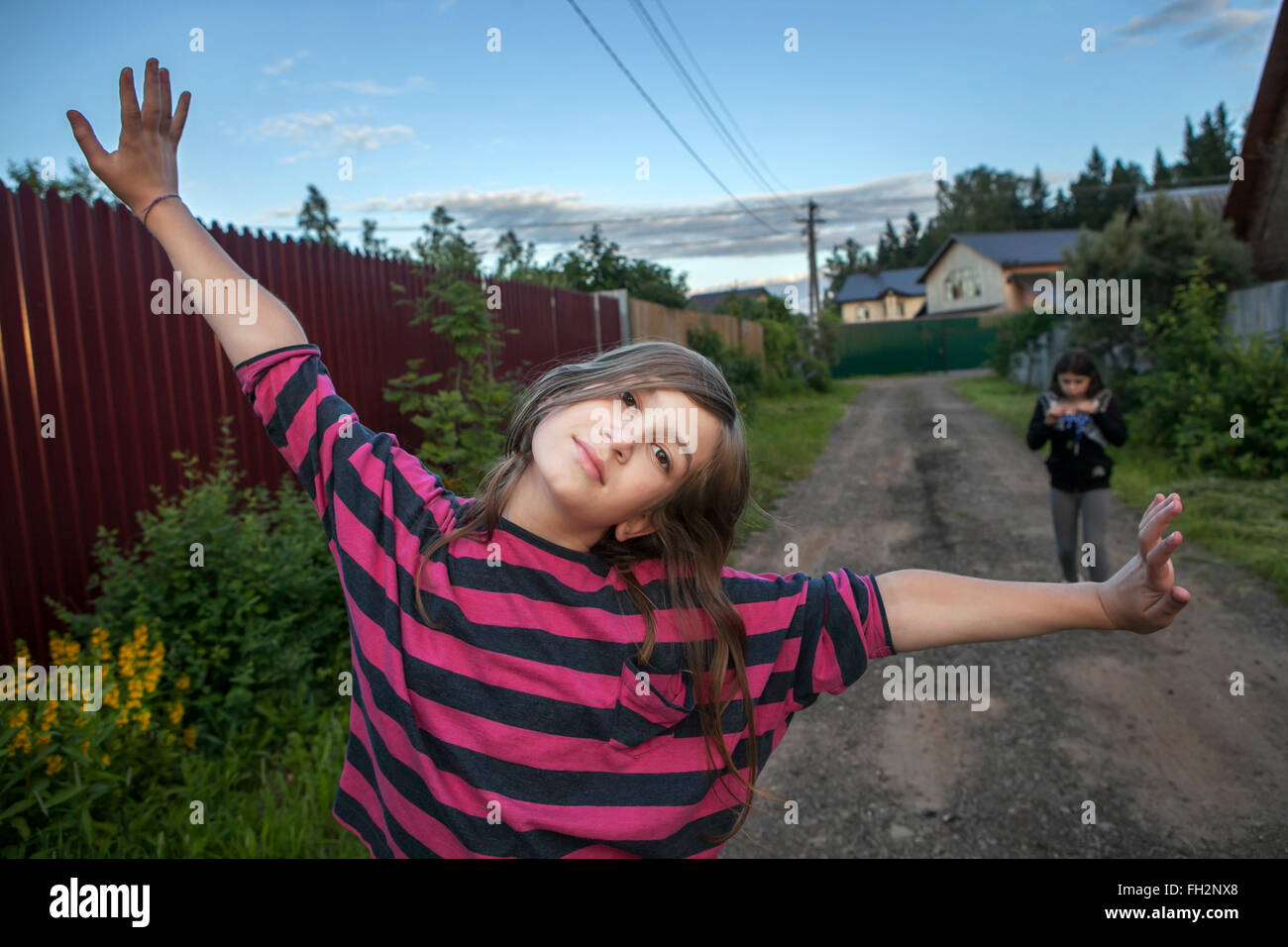 Sorridente ragazza adolescente in un rosso striped shirt permanente sulla strada tra le case, le braccia al cielo. Foto Stock