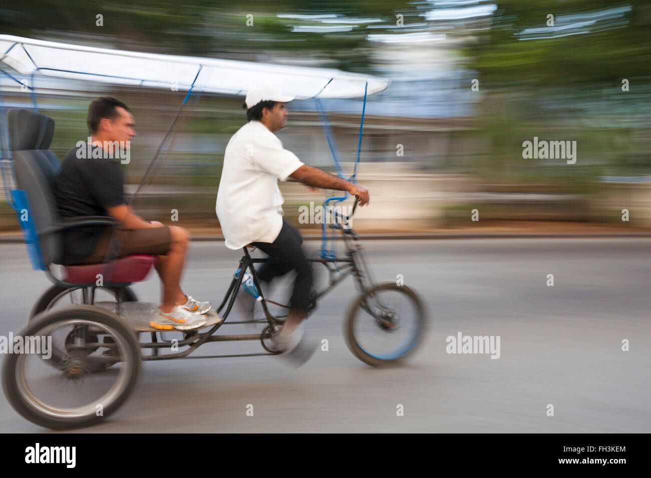 La vita quotidiana a Cuba - bicitaxi taxi bicicletta accelerando lungo la strada di El Malecon, Havana, Cuba, West Indies, dei Caraibi e America centrale Foto Stock