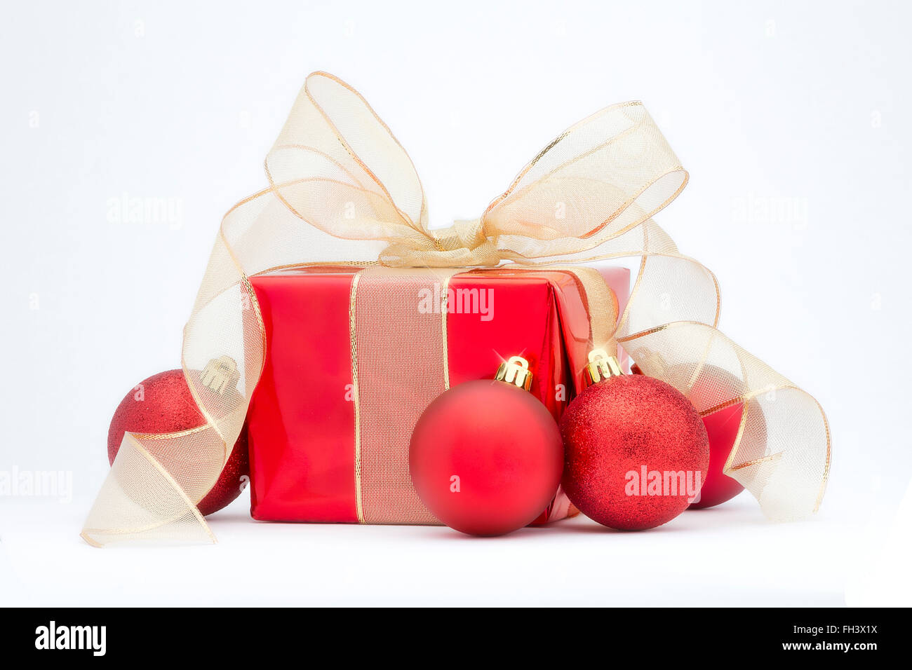 In rosso di un regalo di Natale con nastro color oro e rosso addobbi per l'albero isolato su uno sfondo bianco. Foto Stock