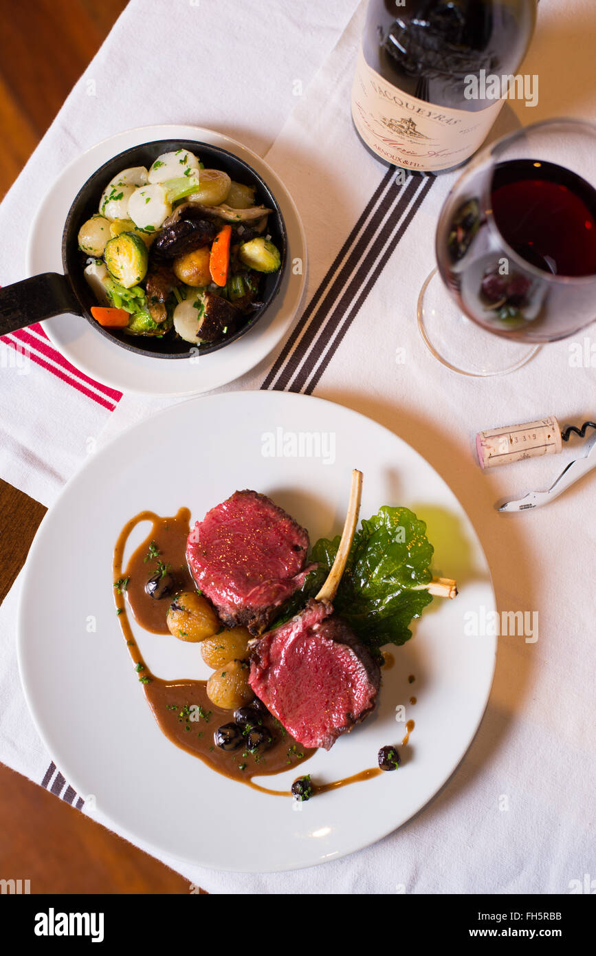 Vista aerea di costolette di agnello su un round piastra bianca con un lato di verdure grigliate e un bicchiere di vino in un ristorante di impostazione Foto Stock