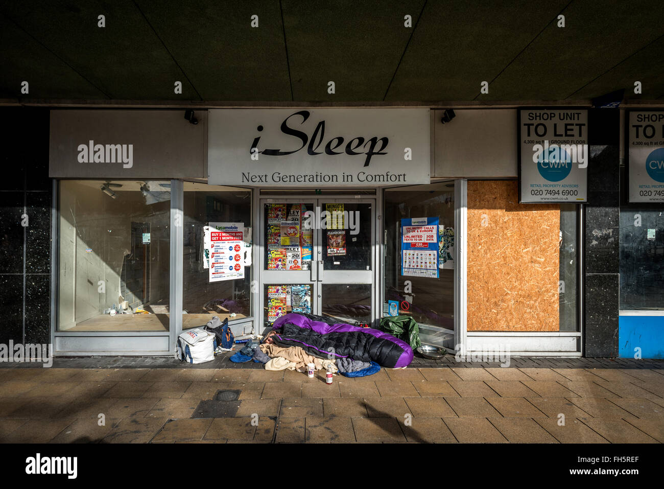 Una persona senza dimora che dorme nella porta di una chiusura-down bedding shop in Crawley, West Sussex. Foto Stock