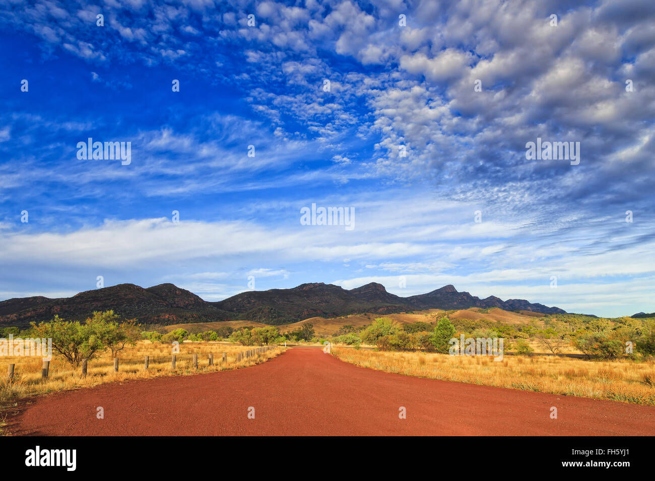 Rosso di strada sterrata verso il Parco Nazionale di Flinders Ranges - la sua Weilpena pound mountain range. Caldo sole di luce a sunris con blue Foto Stock