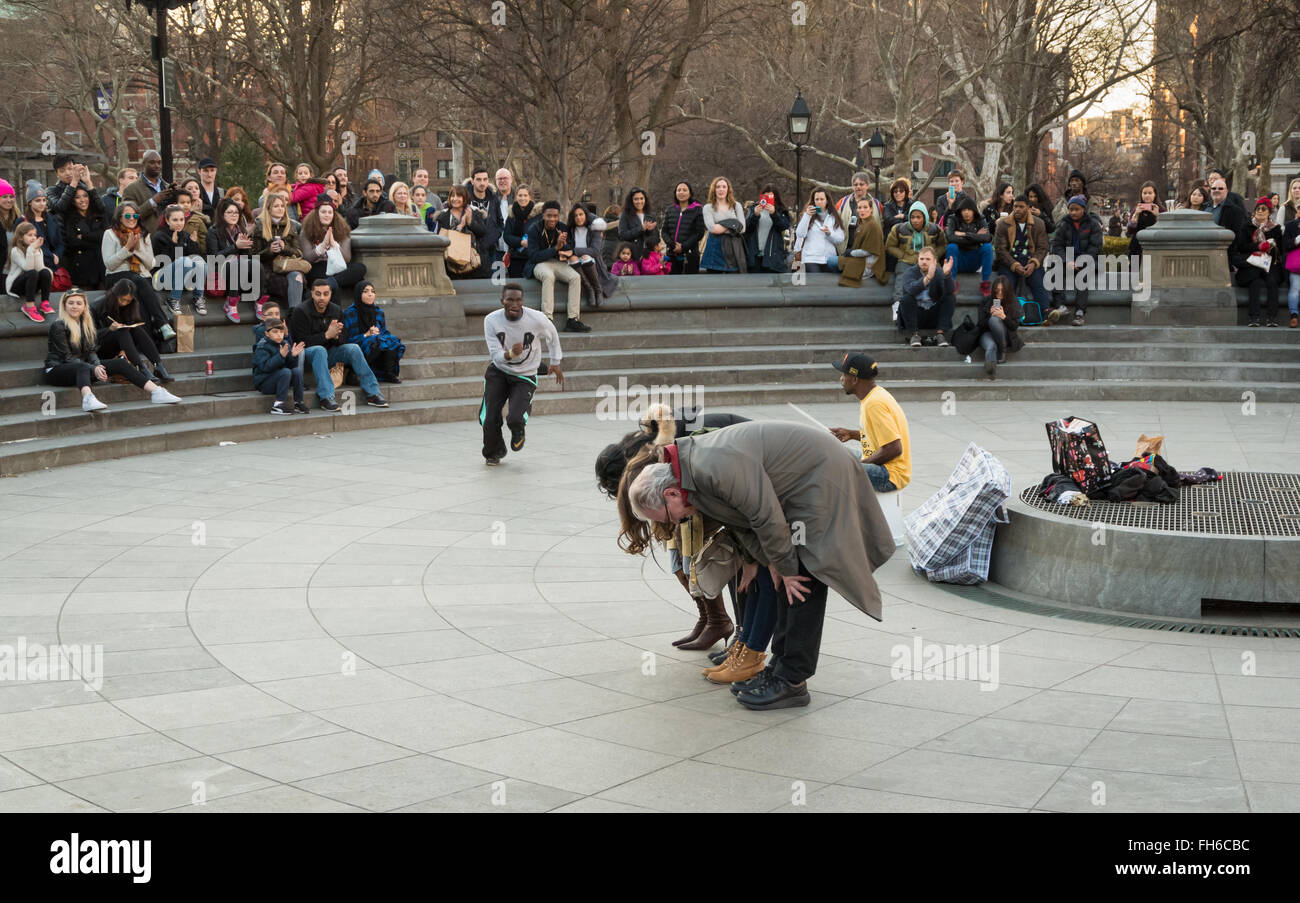 Street performance in Washington Square Park di acrobat somersaulting su volontari con la folla di spettatori Foto Stock