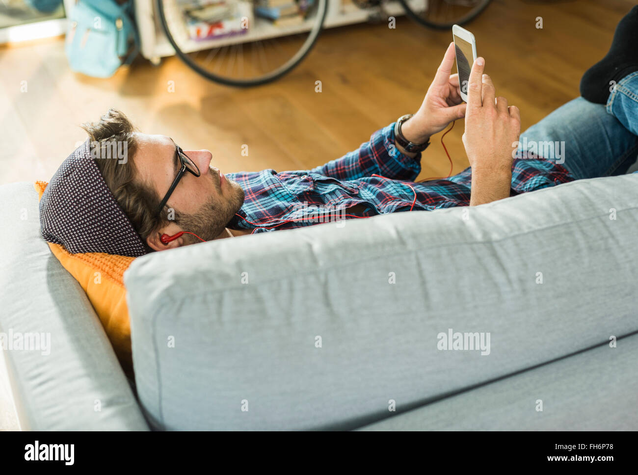 Giovane uomo disteso sul lettino ascolto della musica con gli auricolari e lo smartphone Foto Stock