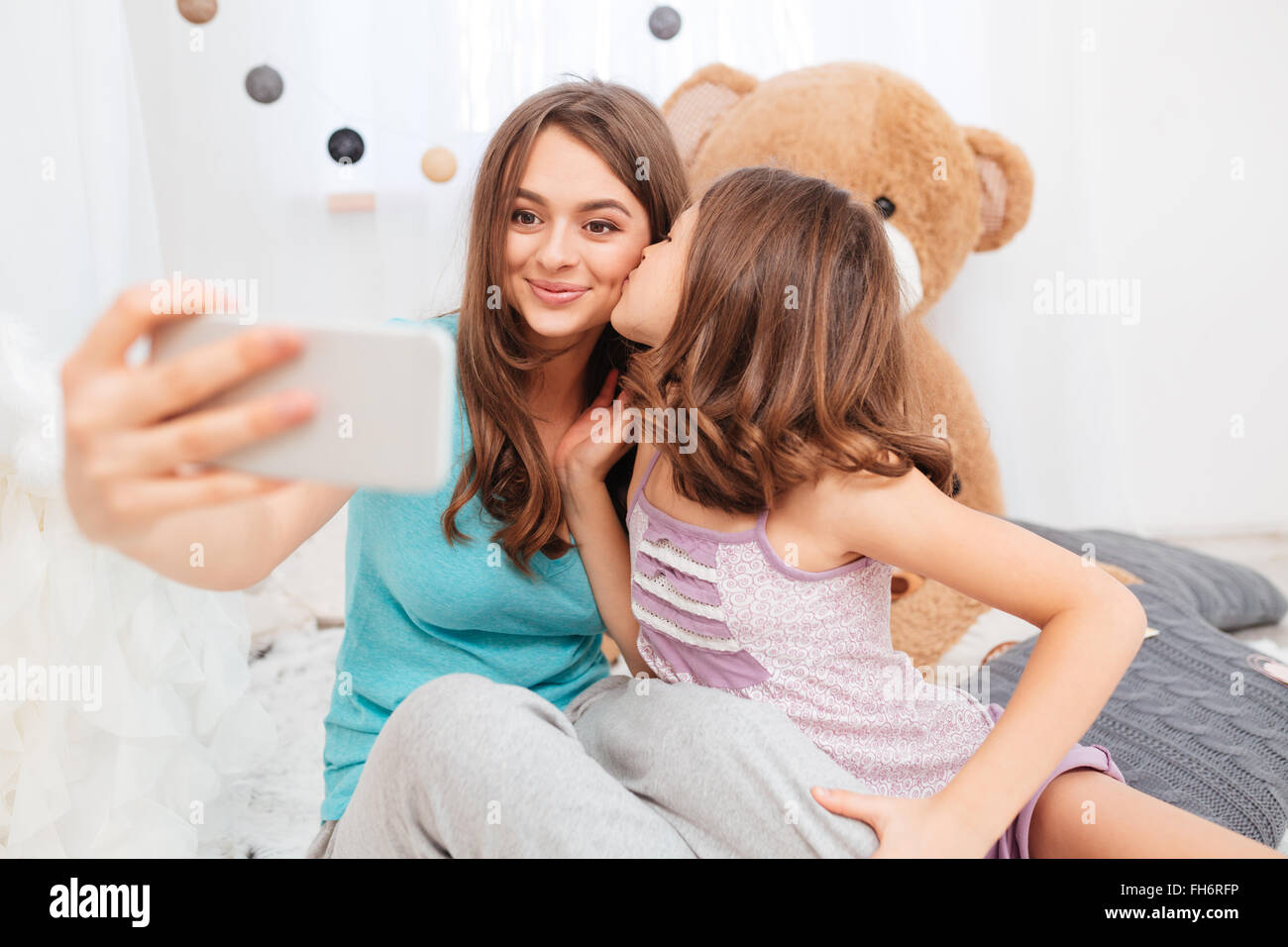 Due graziose sorelle sorridente baciare e rendendo selfie in camera per bambini Foto Stock