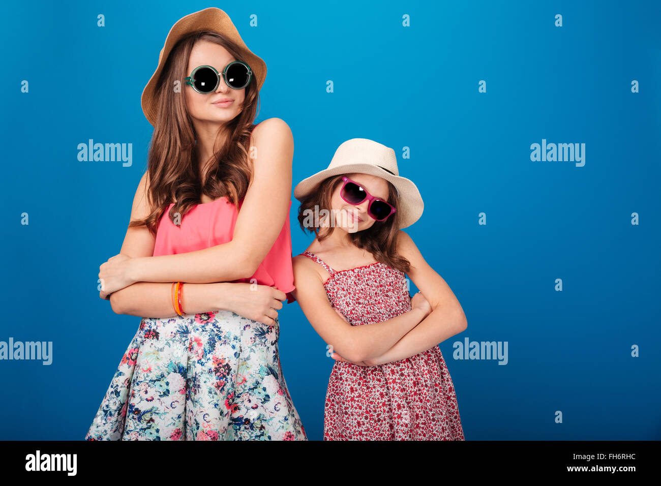 Due graziose sorelle sorridente in piedi e in posa con mani ripiegata su sfondo blu Foto Stock