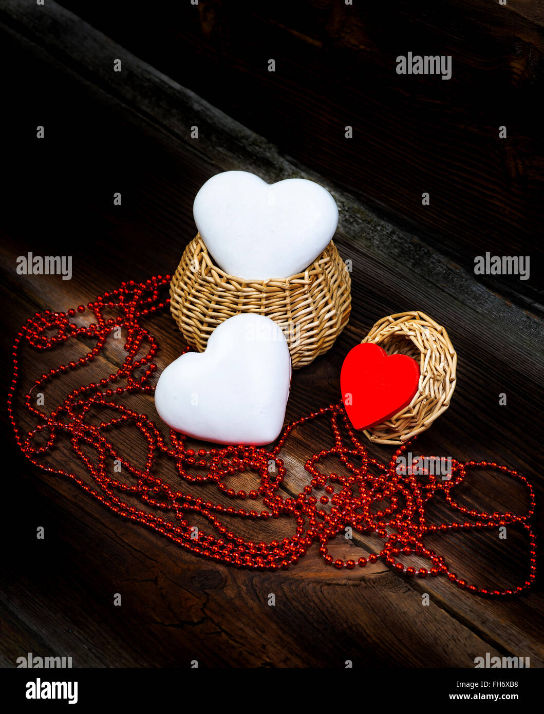 Cuori, Piccolo cesto in legno e filo di perle rosso sul vecchio di tavole di legno. Composizione di amore. Foto Stock