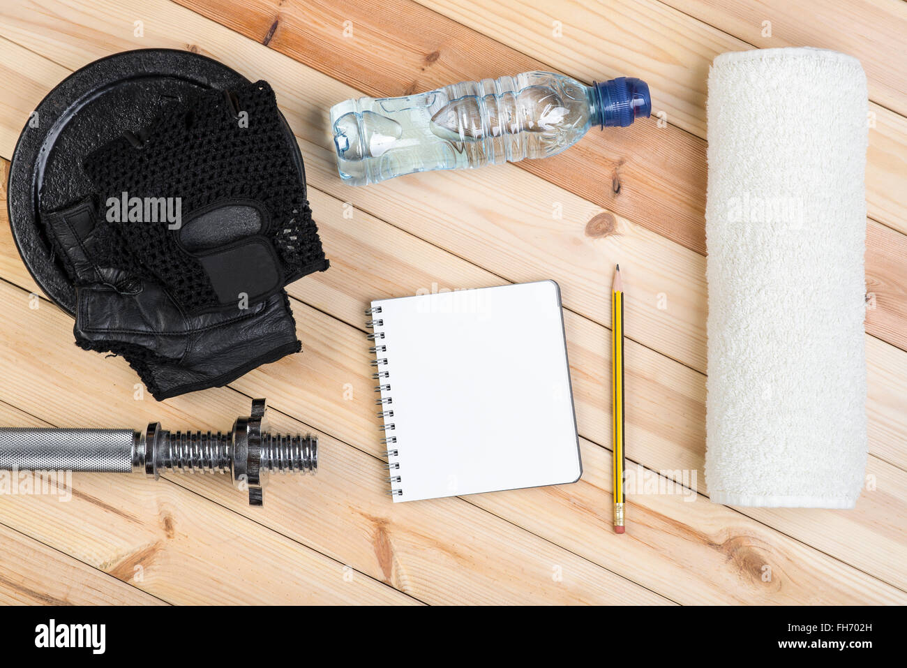 Sport Concept. Barbell, Peso, guanti, asciugamano, bottiglia di acqua e il notebook al piano di allenamento su un tavolo di legno. Foto Stock