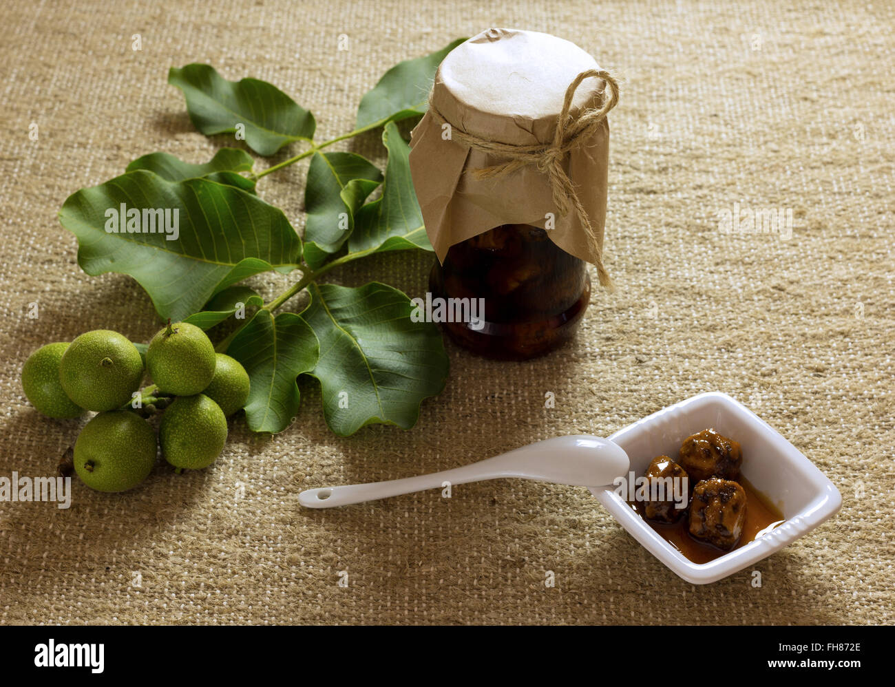 Vasetto di marmellata dadi sulla tela a trama con foglie e frutta, bianco piastra ceramica e cucchiaio Foto Stock