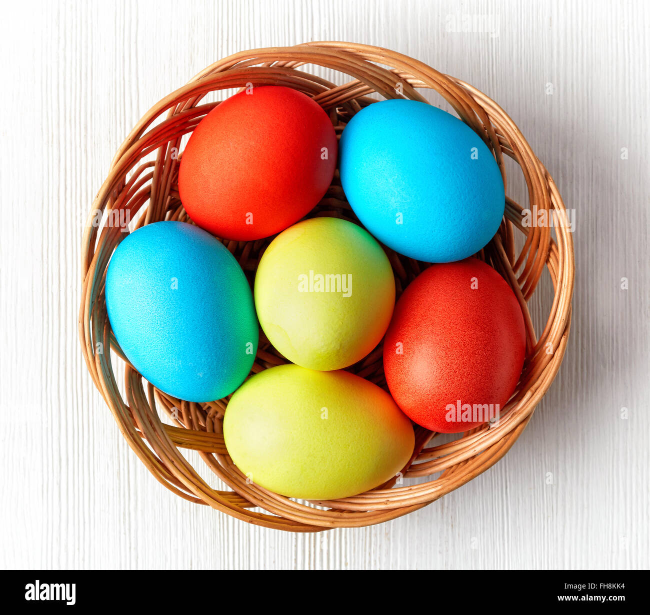 Uova di Pasqua in un cesto di vimini su sfondo bianco, vista dall'alto Foto Stock