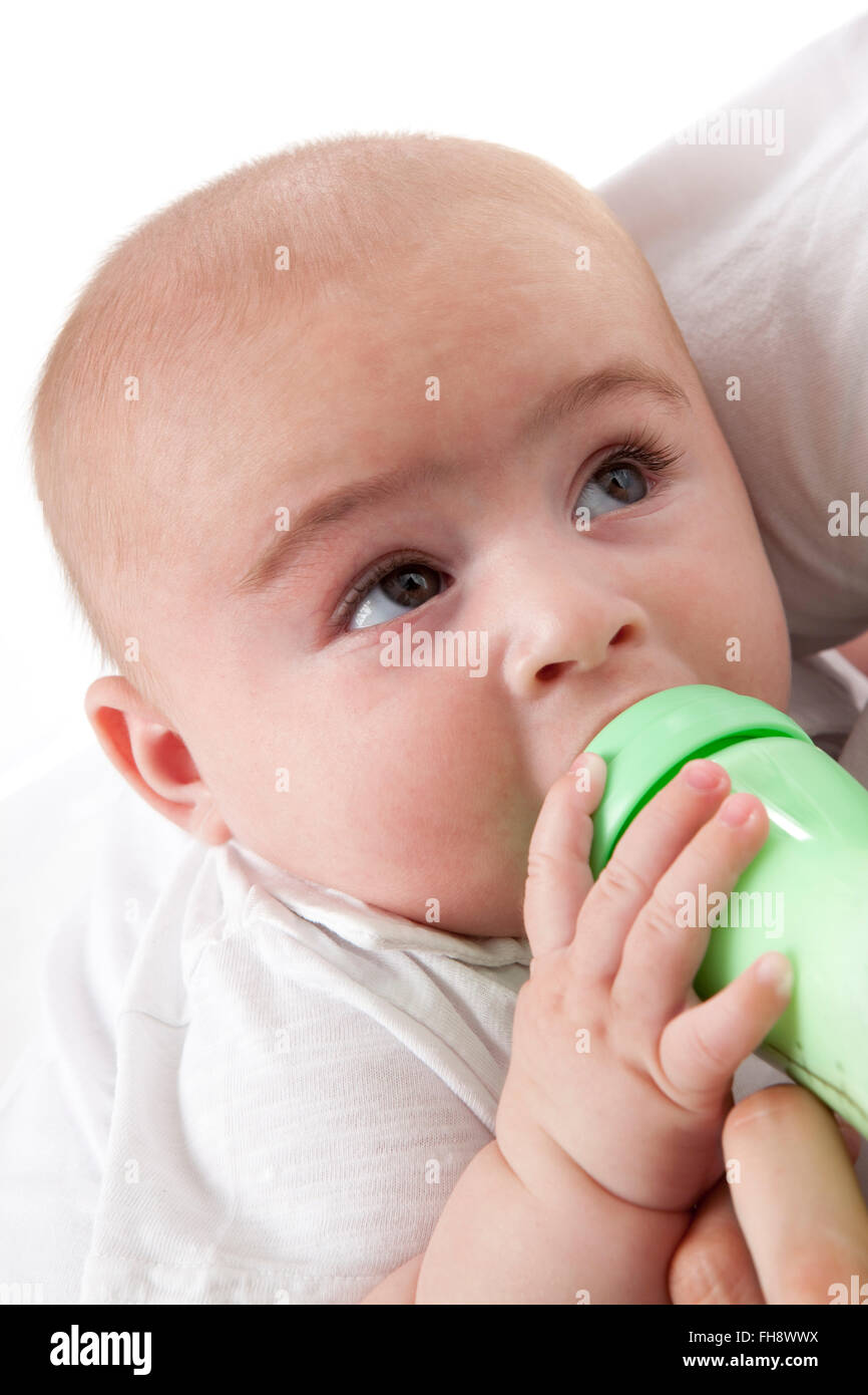 Bambino guardando i suoi genitori mentre si beve da un biberon su sfondo bianco Foto Stock
