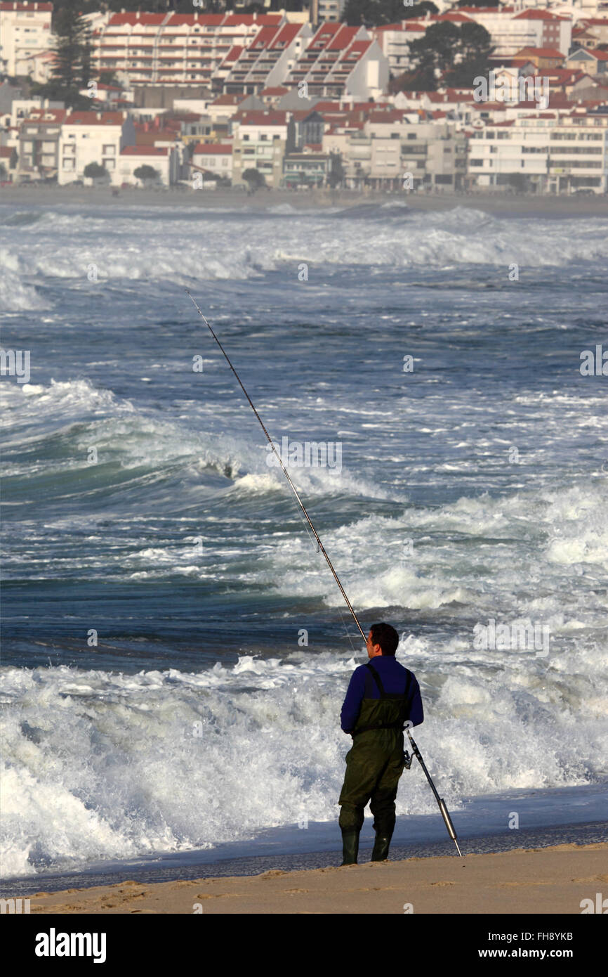 L'uomo della pesca in mare dalla spiaggia sabbiosa, Vila Praia de ancora in background, Provincia del Minho, Portogallo settentrionale Foto Stock