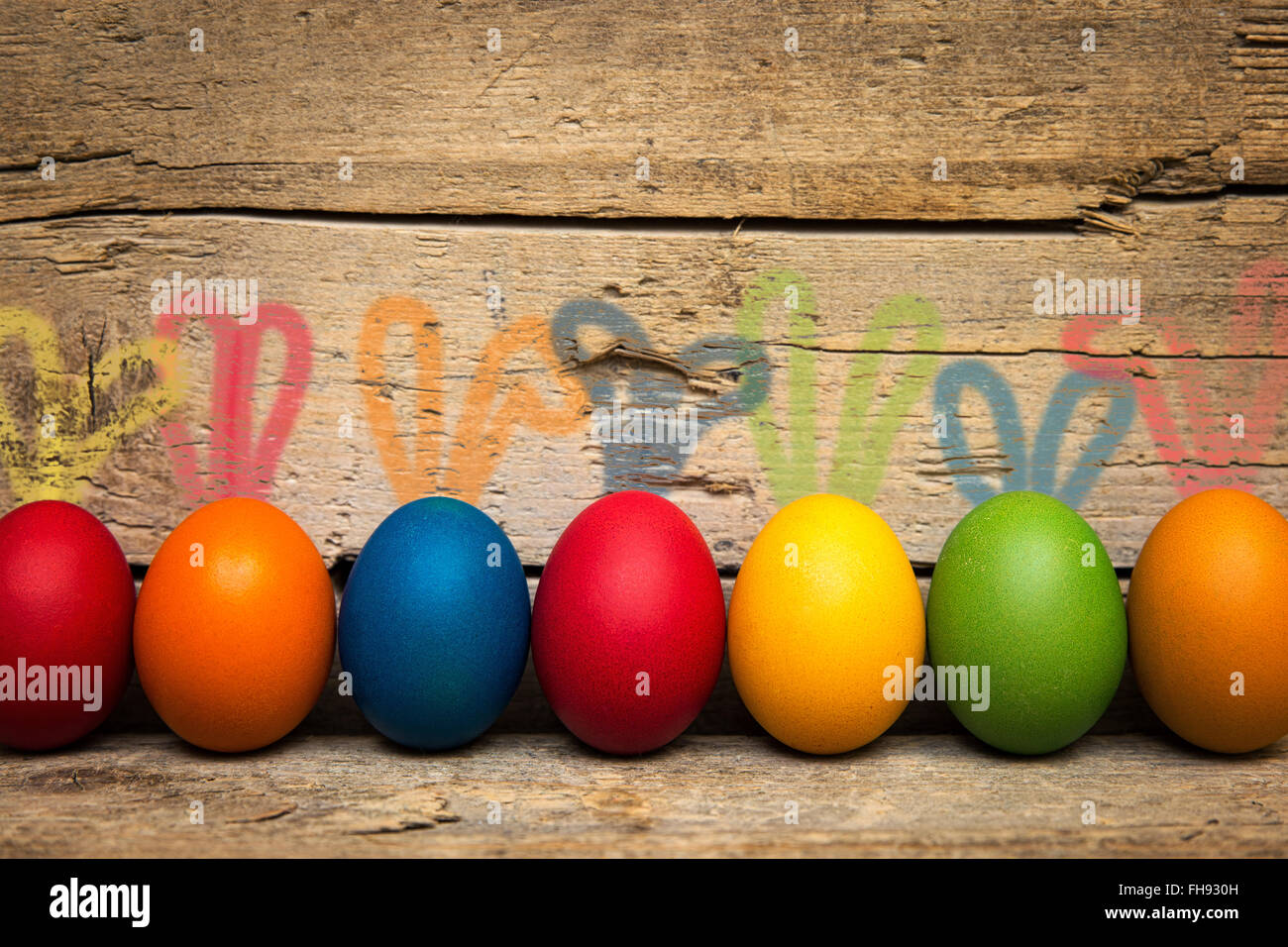 Divertente colorato le uova di pasqua con orecchie di coniglio, di fronte a uno sfondo di legno Foto Stock