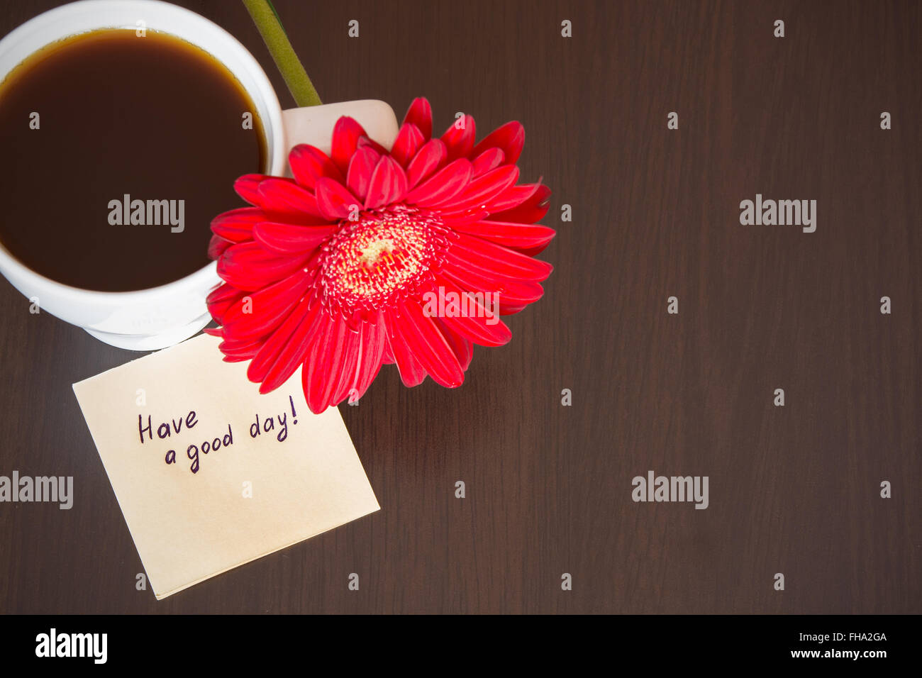 Rosso fiore di gerbera, una tazza di caffè e la carta con testo ''hanno una buona giornata!" sulla scrivania in legno. Messa a fuoco selettiva, tonica Foto Stock