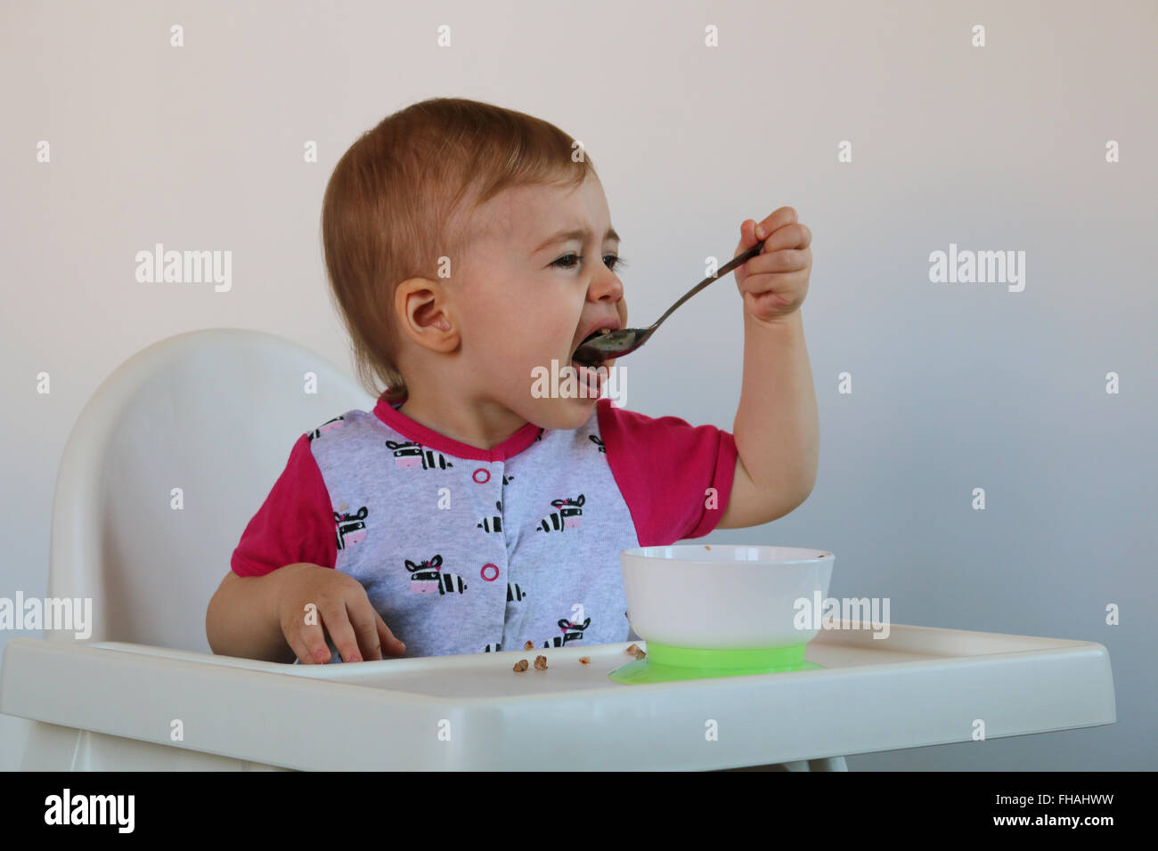 Bambina mangia la crema di farina e di latte si siede su una sedia Foto Stock