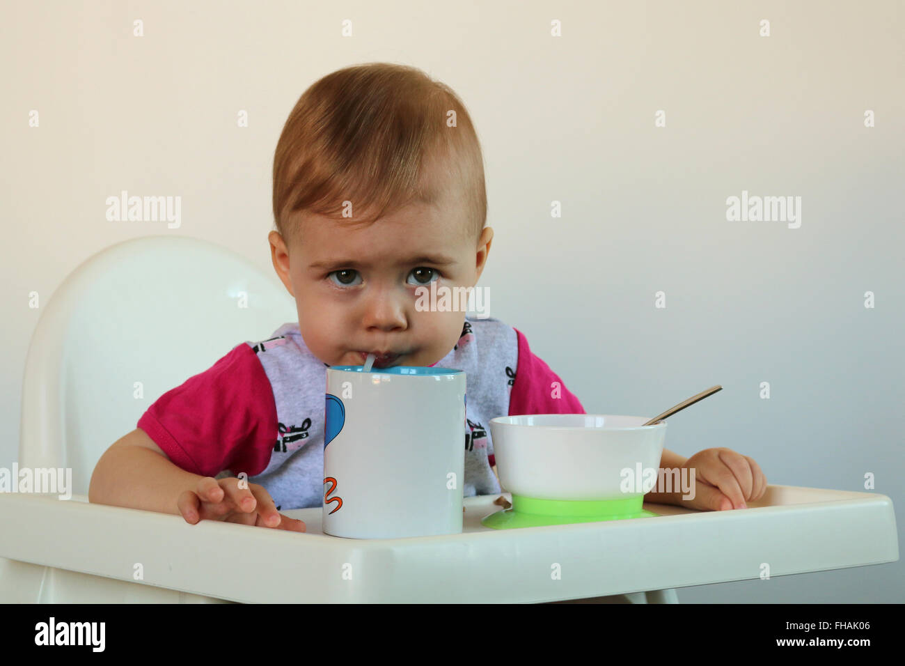 Piccolo bambino beve acqua seduta sul seggiolone Foto Stock