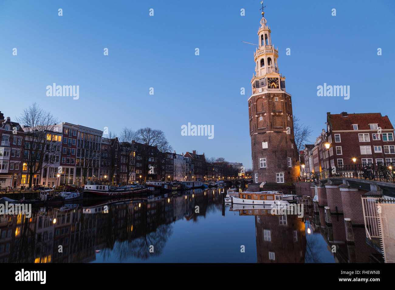 Una vista lungo il canale Oudeschans verso la Torre Montelbaanstoren ad Amsterdam al crepuscolo. Edificio, barche e riflessioni Foto Stock