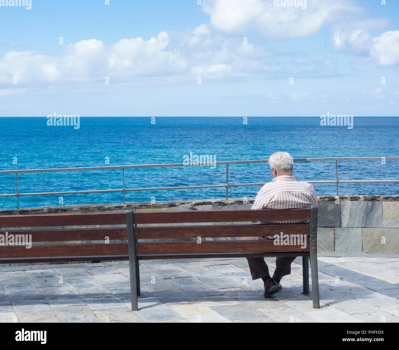 Il vecchio uomo seduto su un banco di lavoro che guarda al mare in Spagna Foto Stock