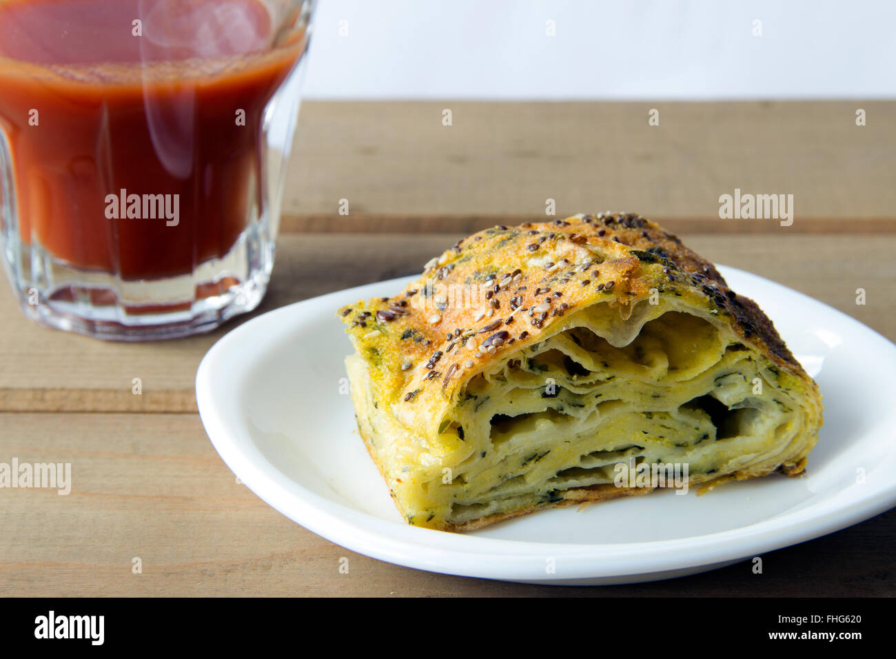 Gli spinaci e torta di formaggio con un bicchiere di succo di pomodoro su una tavola di legno Foto Stock