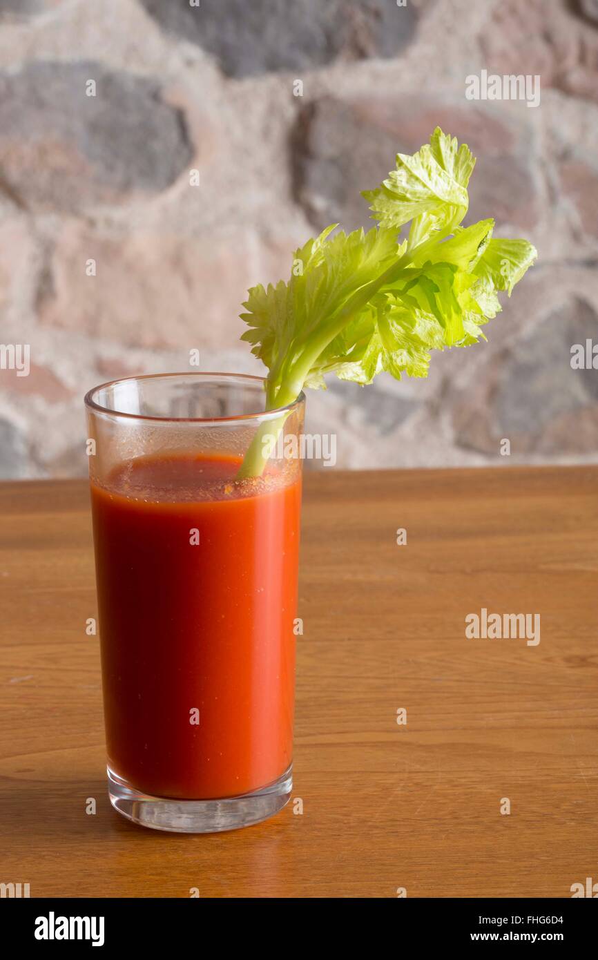 Bicchiere di succo di pomodoro con un gambo di sedano seduto su un tavolo in legno nella parte anteriore di un rustico muro di pietra Foto Stock