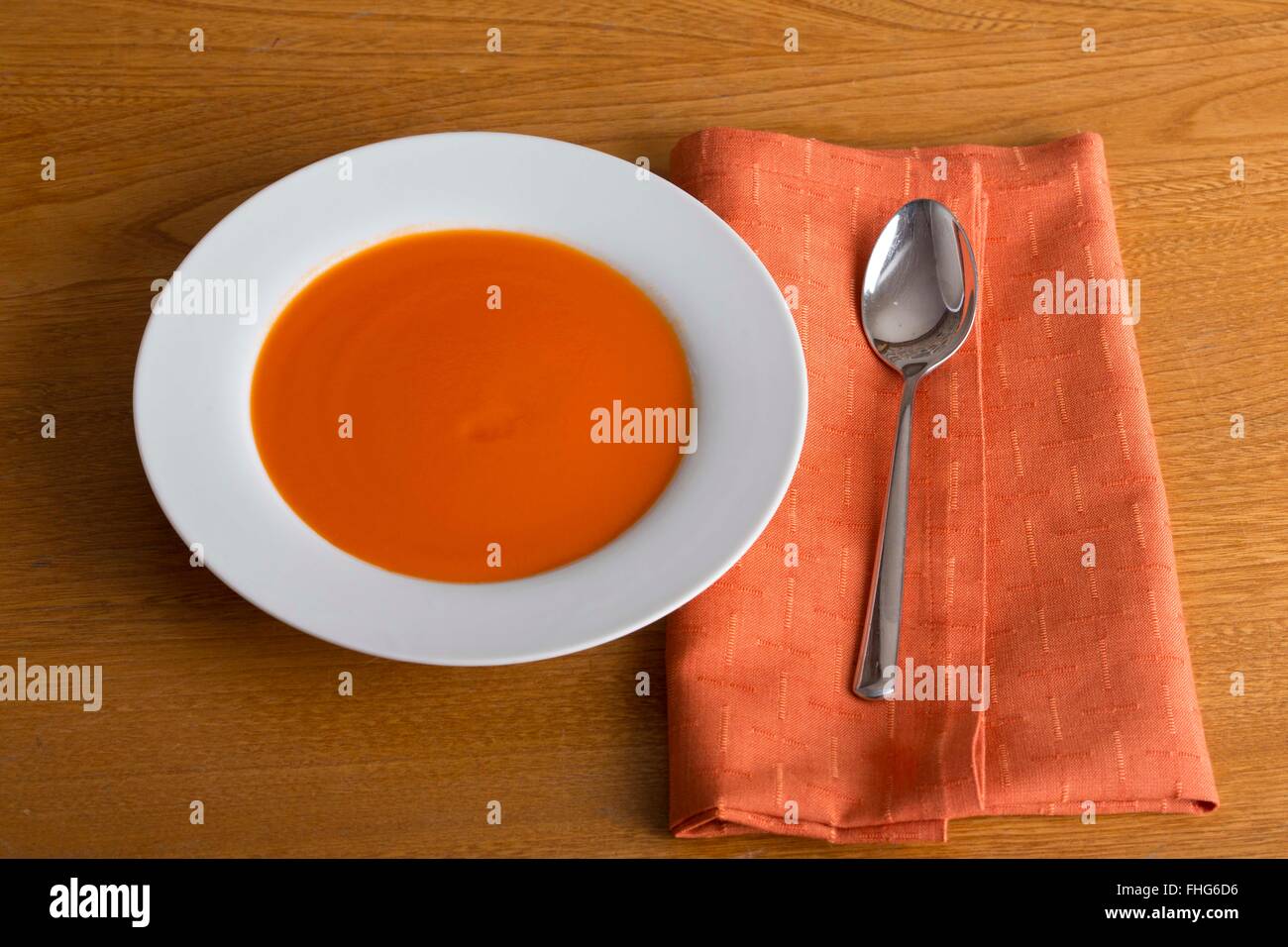 Semplice immagine di una ciotola di zuppa con un cucchiaio e tovagliolo su una cucina in legno Tabella presa da sopra Foto Stock