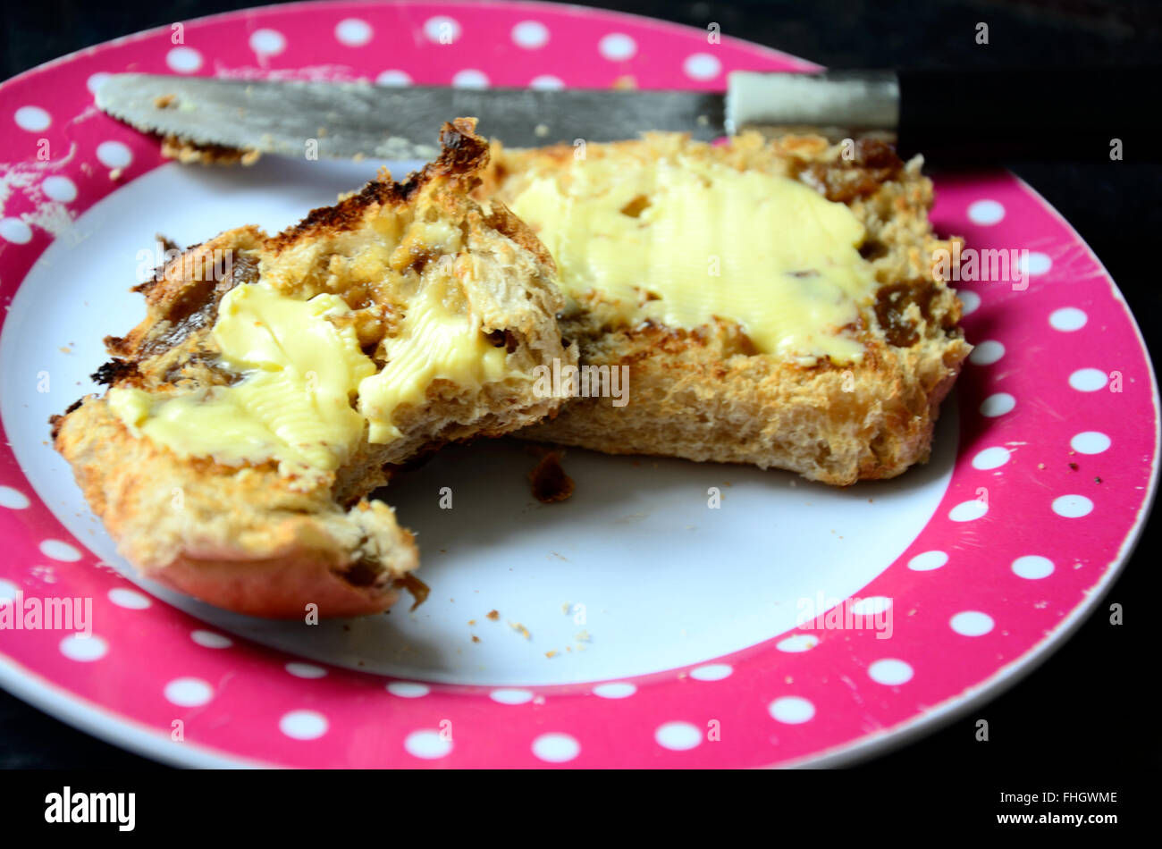 Un hot cross bun, tagliate a metà, tostato e spalmato di burro. Una delle metà ha avuto un morso prelevato. Foto Stock