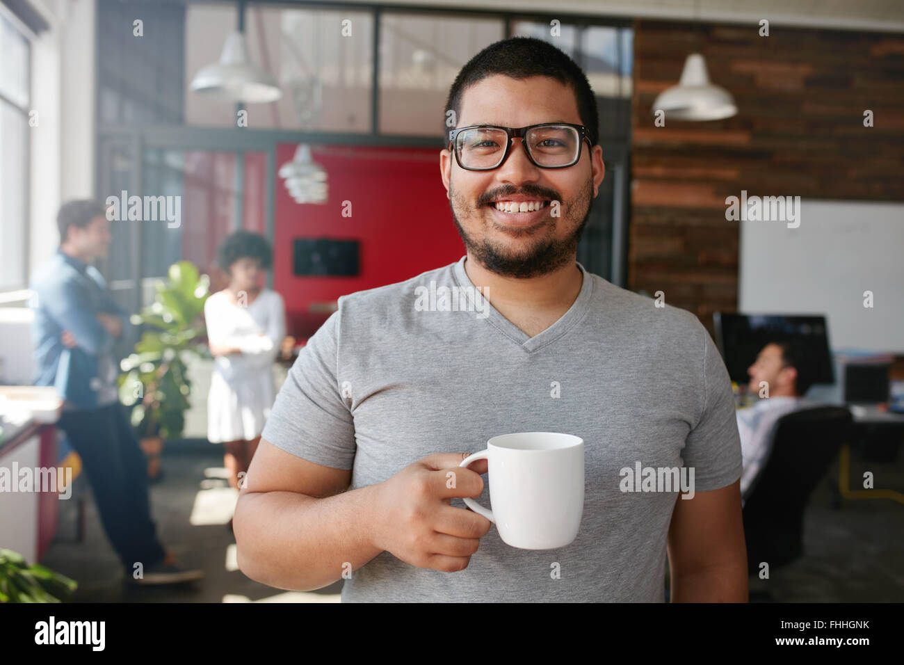 Ritratto di sorridere lavoratore di ufficio avente un caffè con i suoi colleghi parlavano in background. Foto Stock