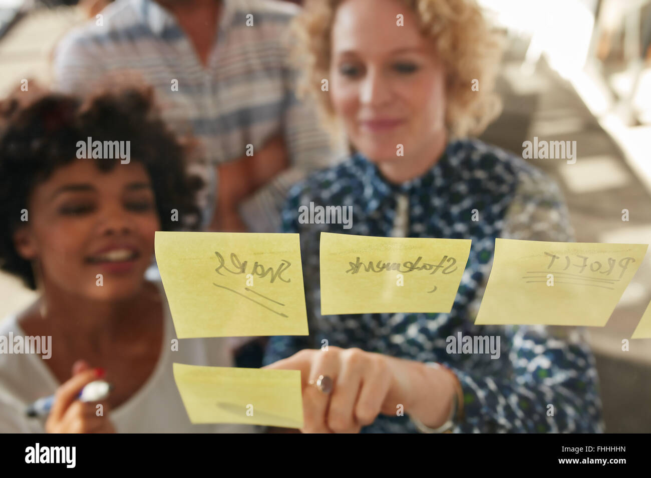Giovane imprenditrice che mostra una sua collega un'idea postato su un foglietto adesivo parete. I professionisti creativi di brainstorming sulle nuove busin Foto Stock