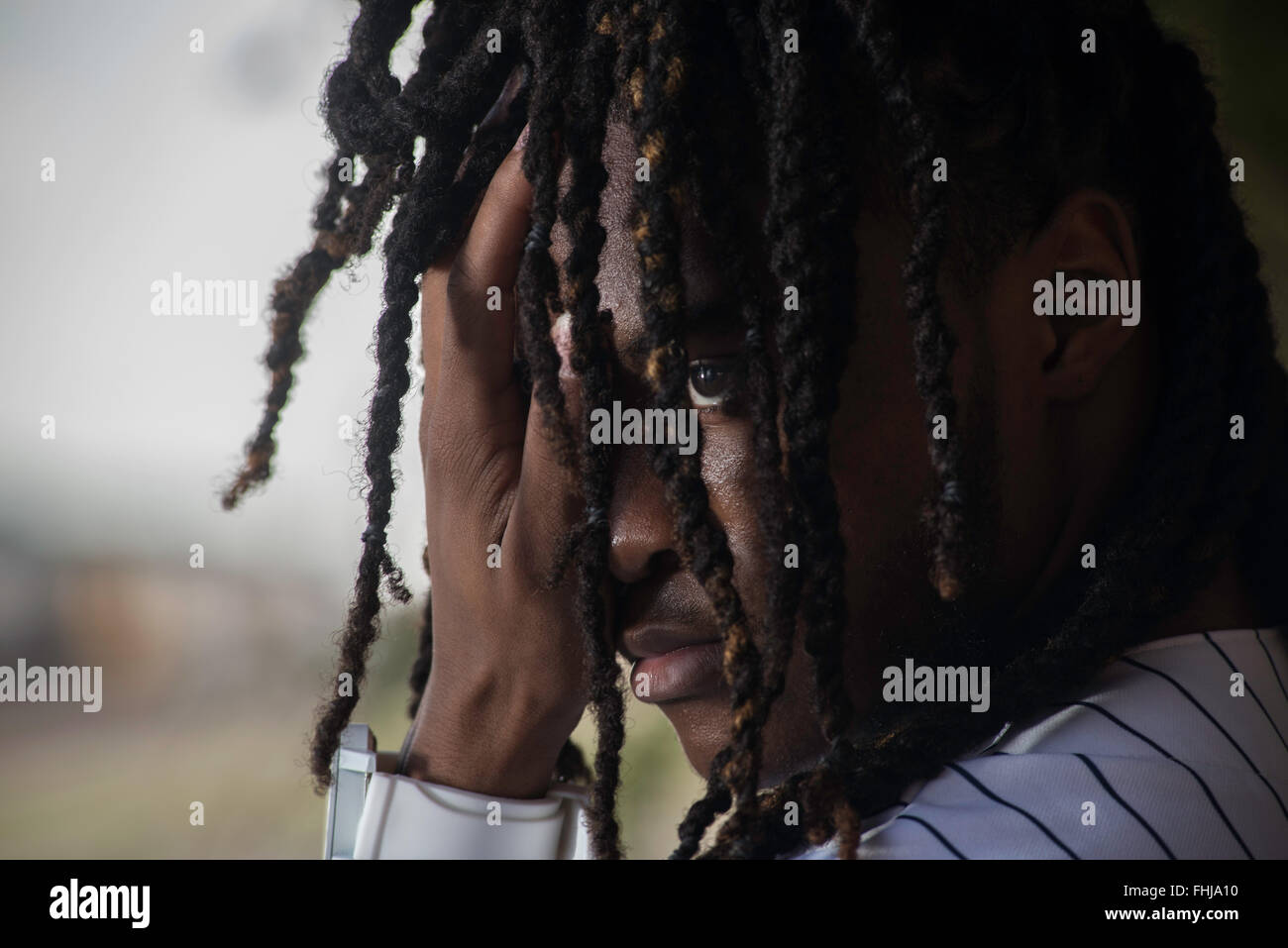 Un afro-americano di adolescente con dreadlocks si erge contro una parete di stagno/siede nel sedile posteriore di un Impala in a junkyard in NC. Foto Stock