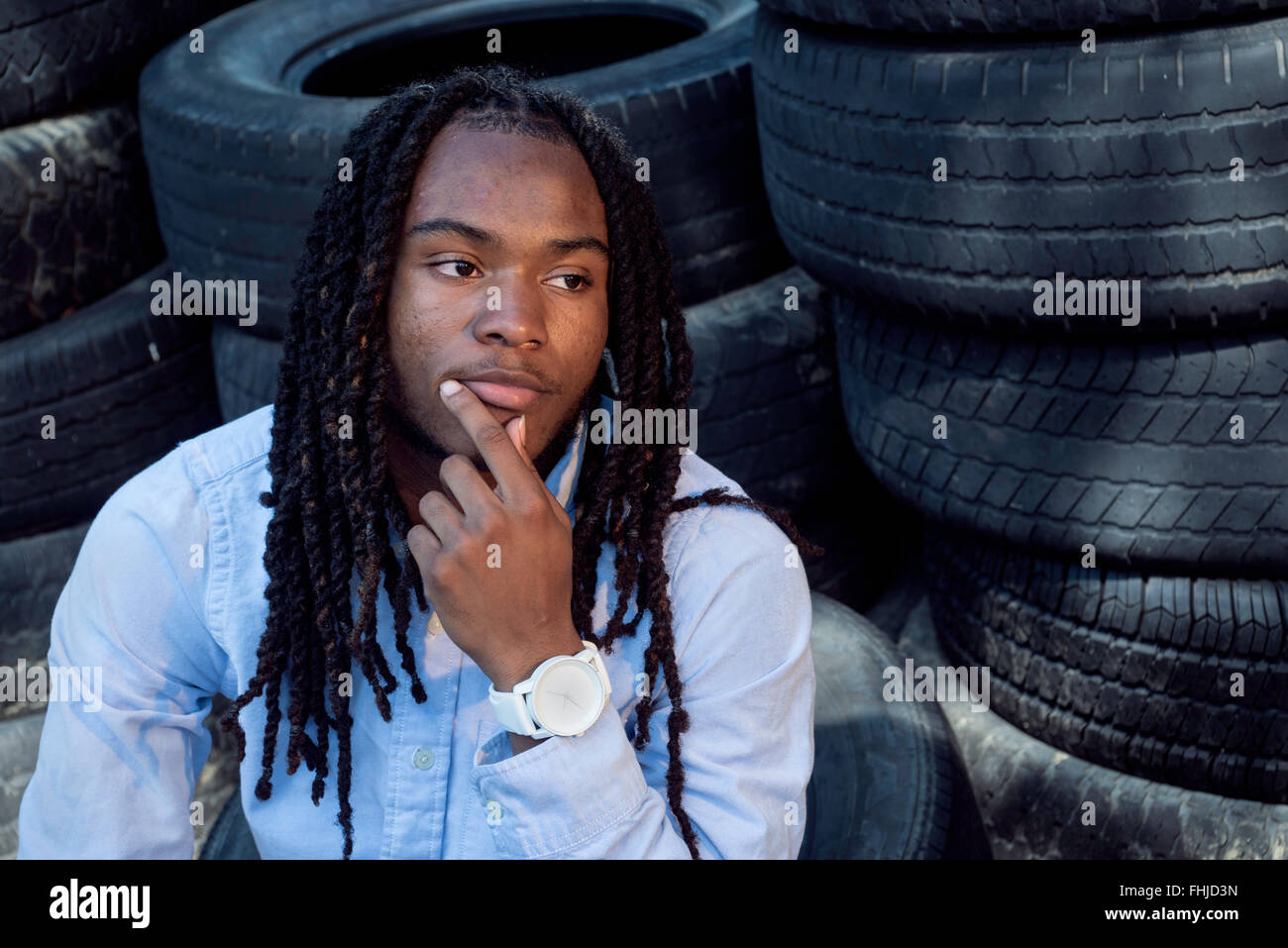 Un afro-americano di adolescente con dreadlocks si erge contro una parete di stagno/siede nel sedile posteriore di un Impala in a junkyard in NC. Foto Stock