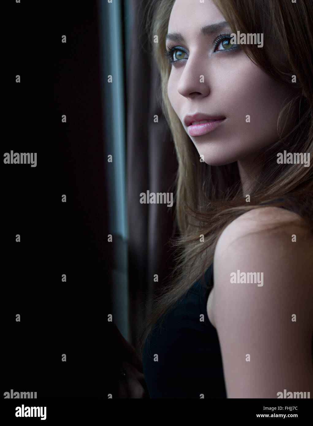 Ritratto di una giovane donna che guarda fuori della finestra Foto Stock
