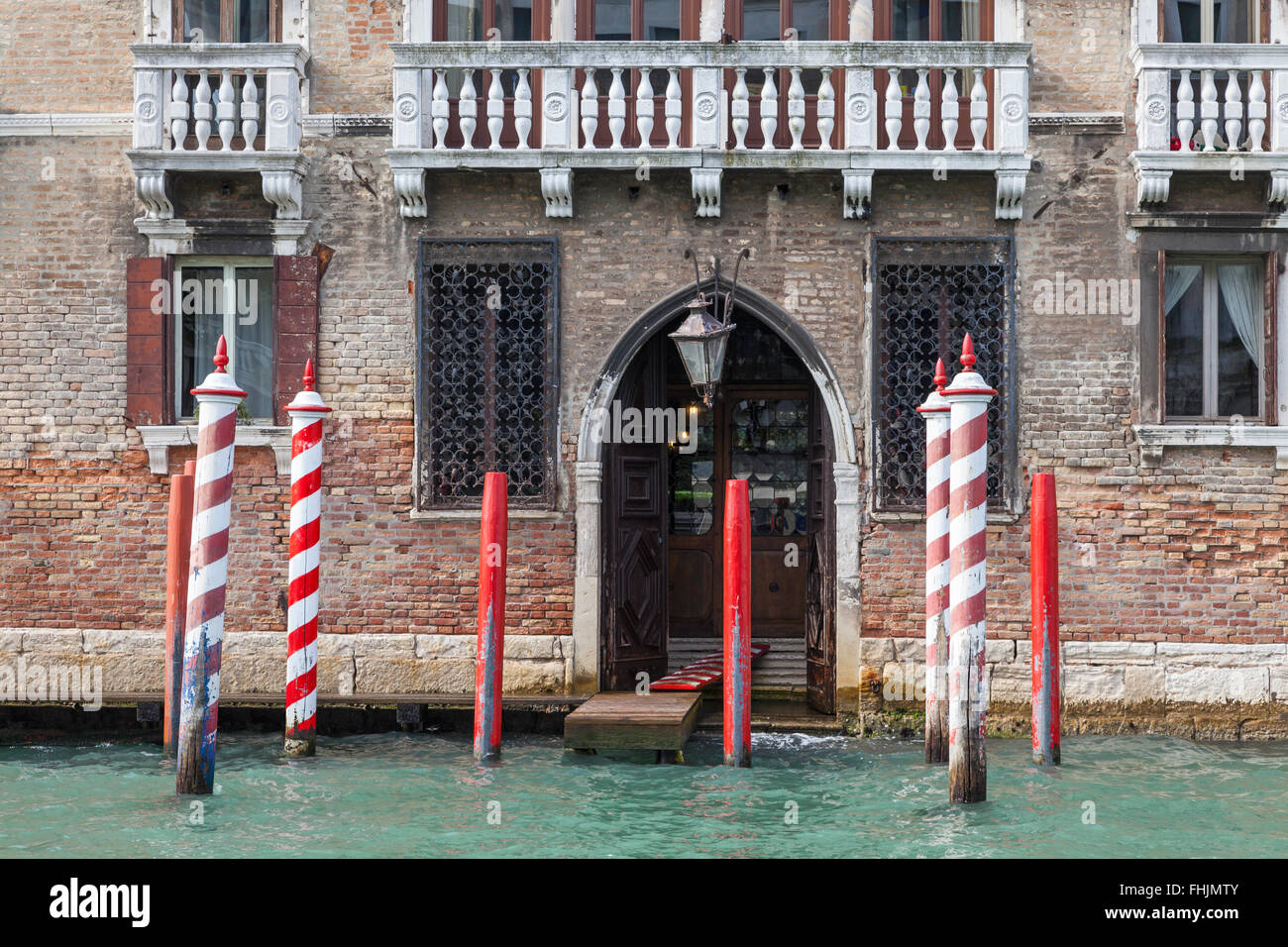 Piano di atterraggio di un vecchio edificio in mattoni con un ingresso ad arco sul Canal Grande, Venezia, con posti d'ormeggio a strisce rosse e bianche Foto Stock