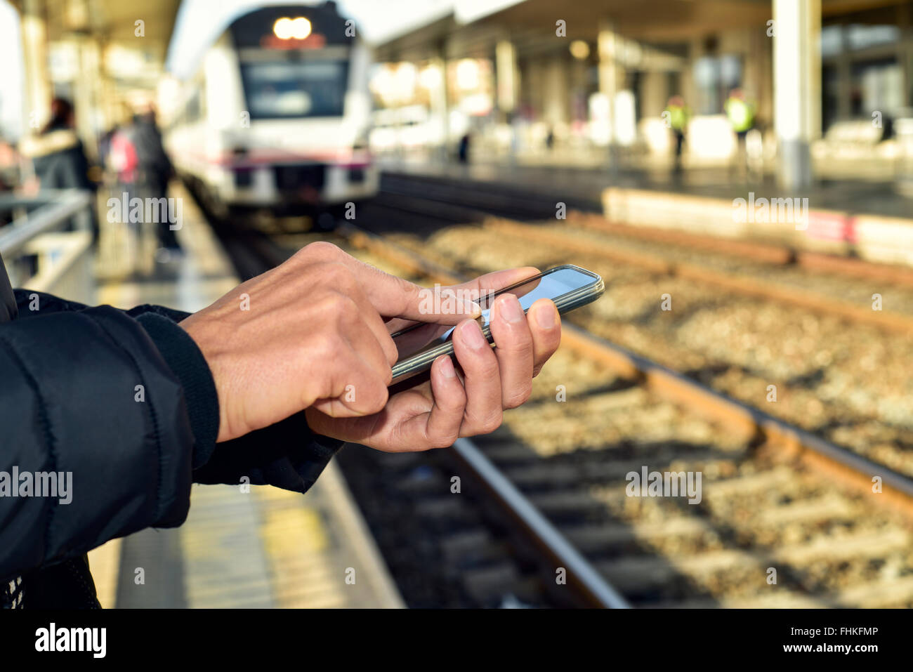 Primo piano di un giovane uomo caucasico utilizzando uno smartphone in un open-air stazione ferroviaria o dalla stazione del tram Foto Stock