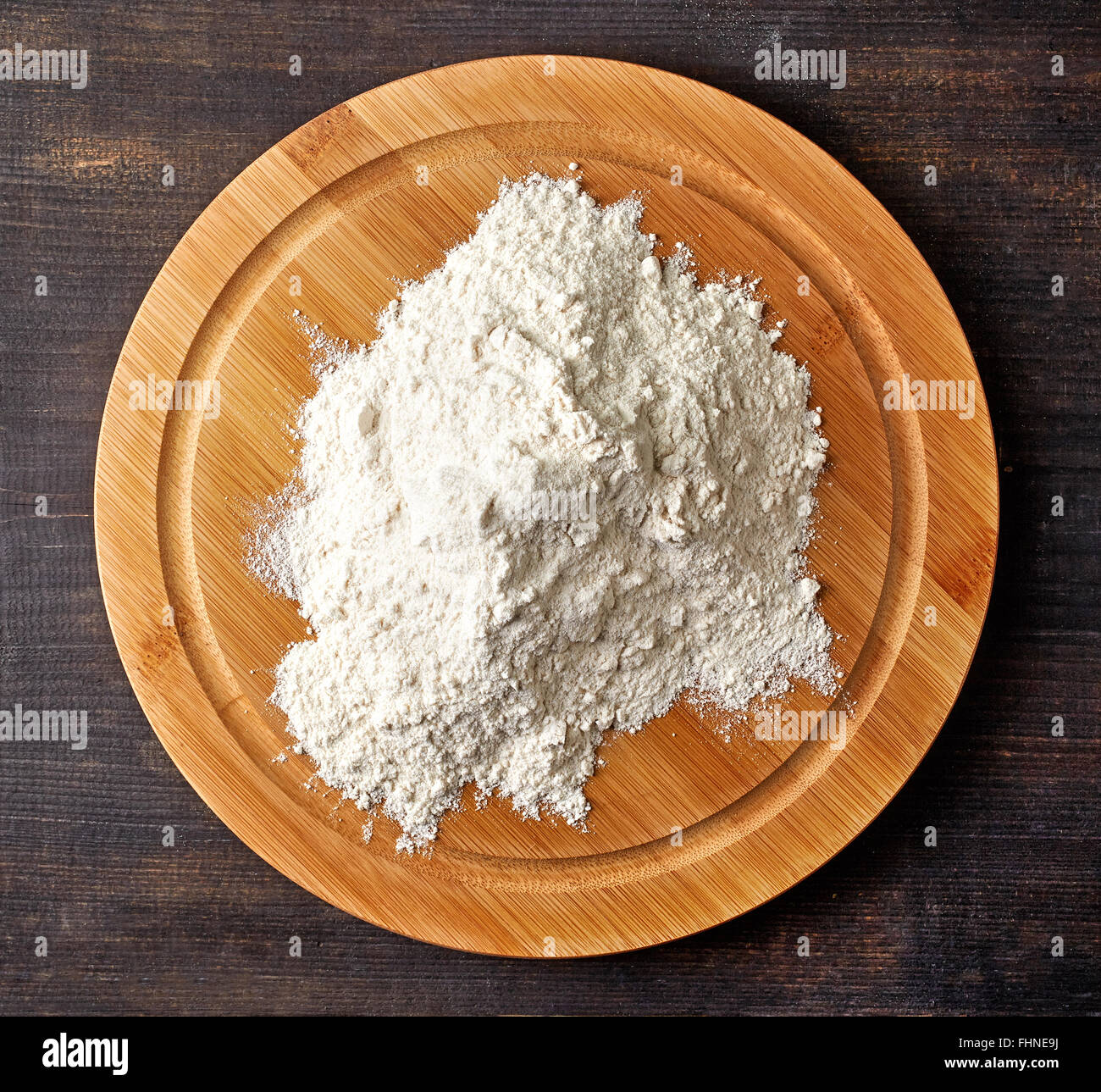 Farina bianca sul round tagliere di legno scuro sul tavolo di legno, vista dall'alto Foto Stock