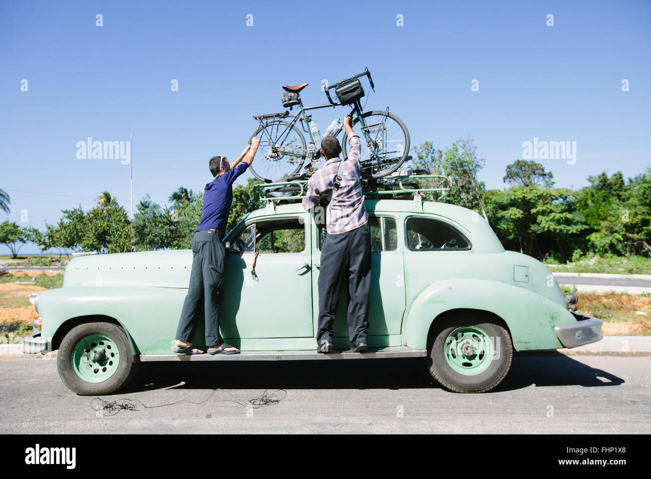 Due uomini caricare una bicicletta sul portapacchi del tetto di un vecchio taxi vintage in Cuba Foto Stock