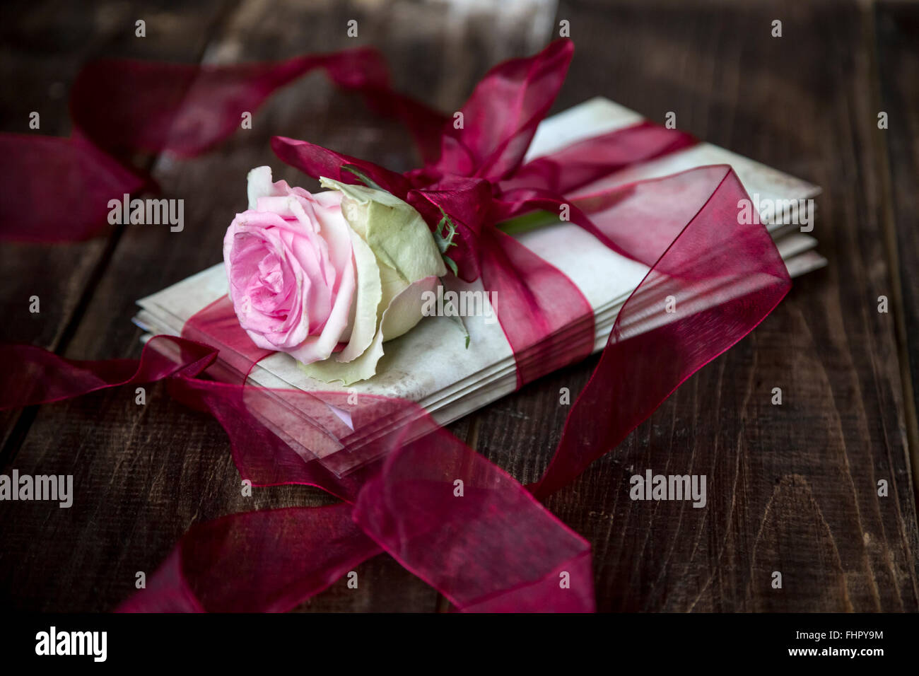 Pila di vecchio amore lettere e bocciolo di rosa legate con un nastro rosso Foto Stock