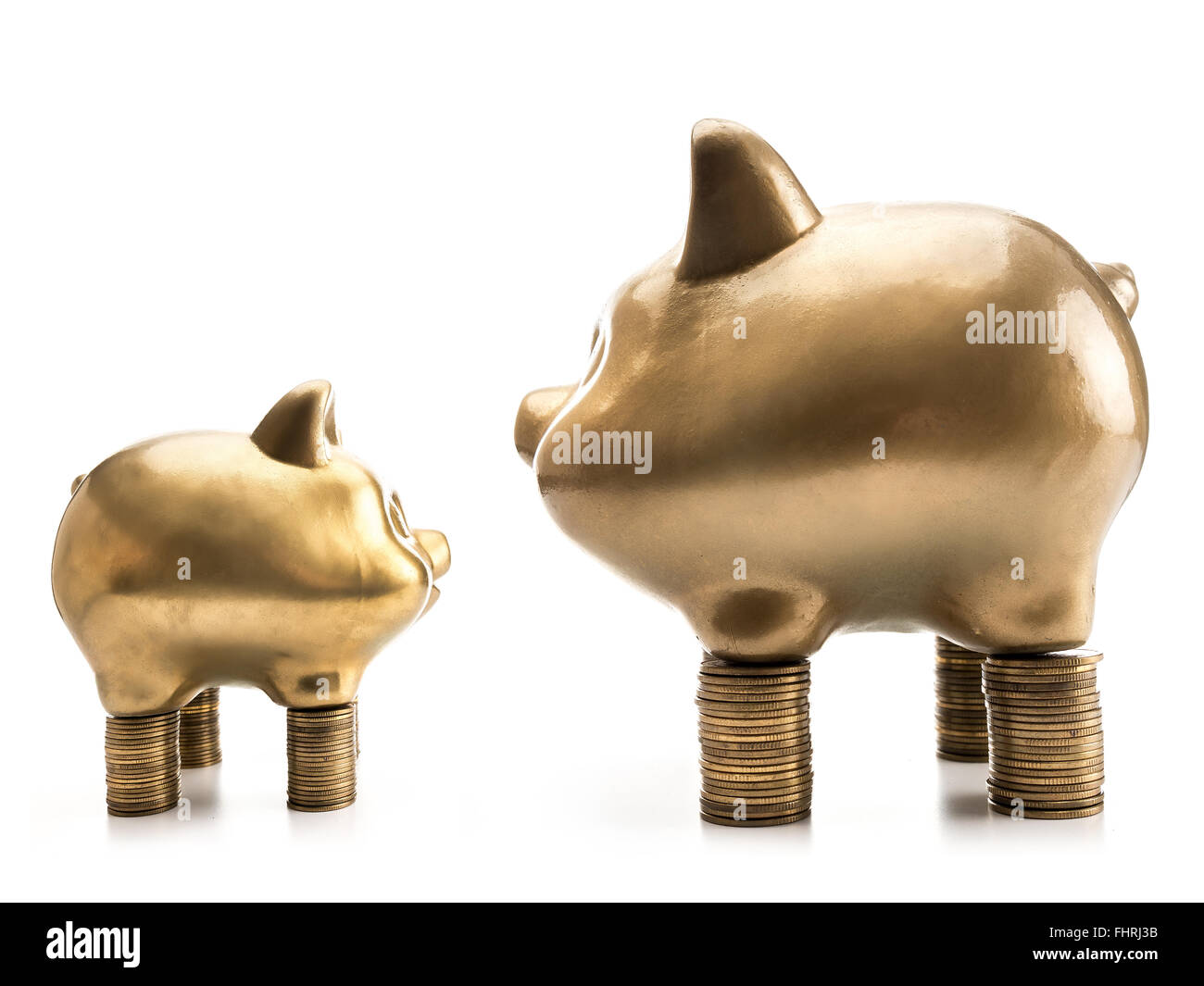 Due grandi e piccoli golden piggybanks in piedi di fronte a ogni altro su pali di denaro su sfondo bianco Foto Stock