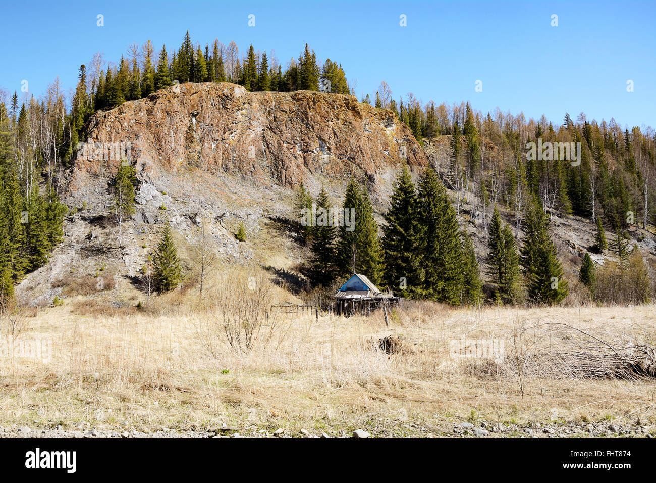 Abbandonato casa in legno sotto una roccia tra le propaggini della catena montuosa di Kuznetsk Alatau. Il Villaggio "foresta". Foto Stock