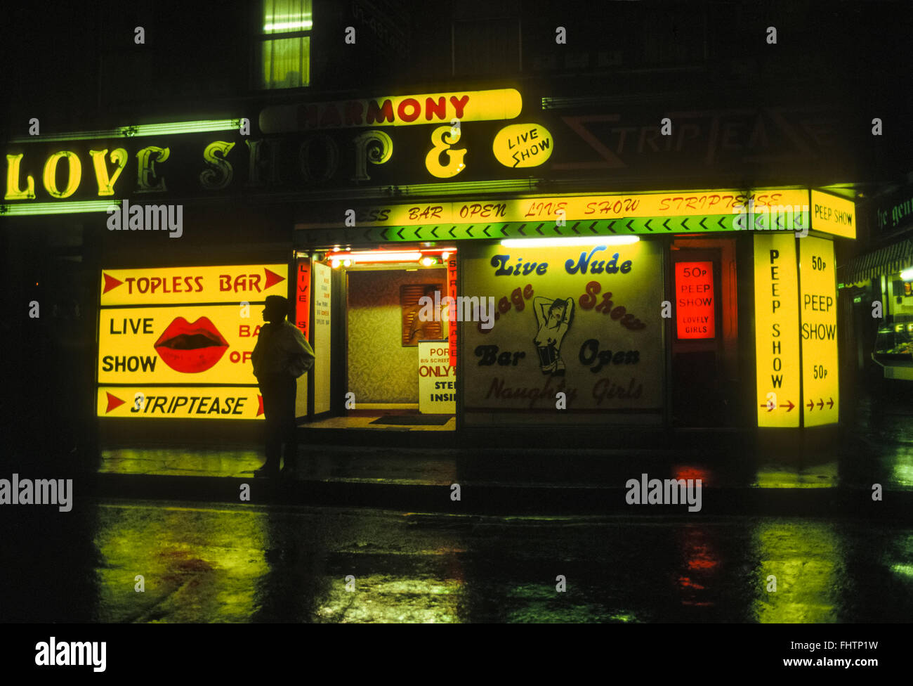 Soho topless bar e peep mostra, strip club insegne al neon riflettendo su strada bagnata, Londra, ottanta. Inghilterra, Regno Unito. Scansione da 35mm trasparenza. Foto Stock