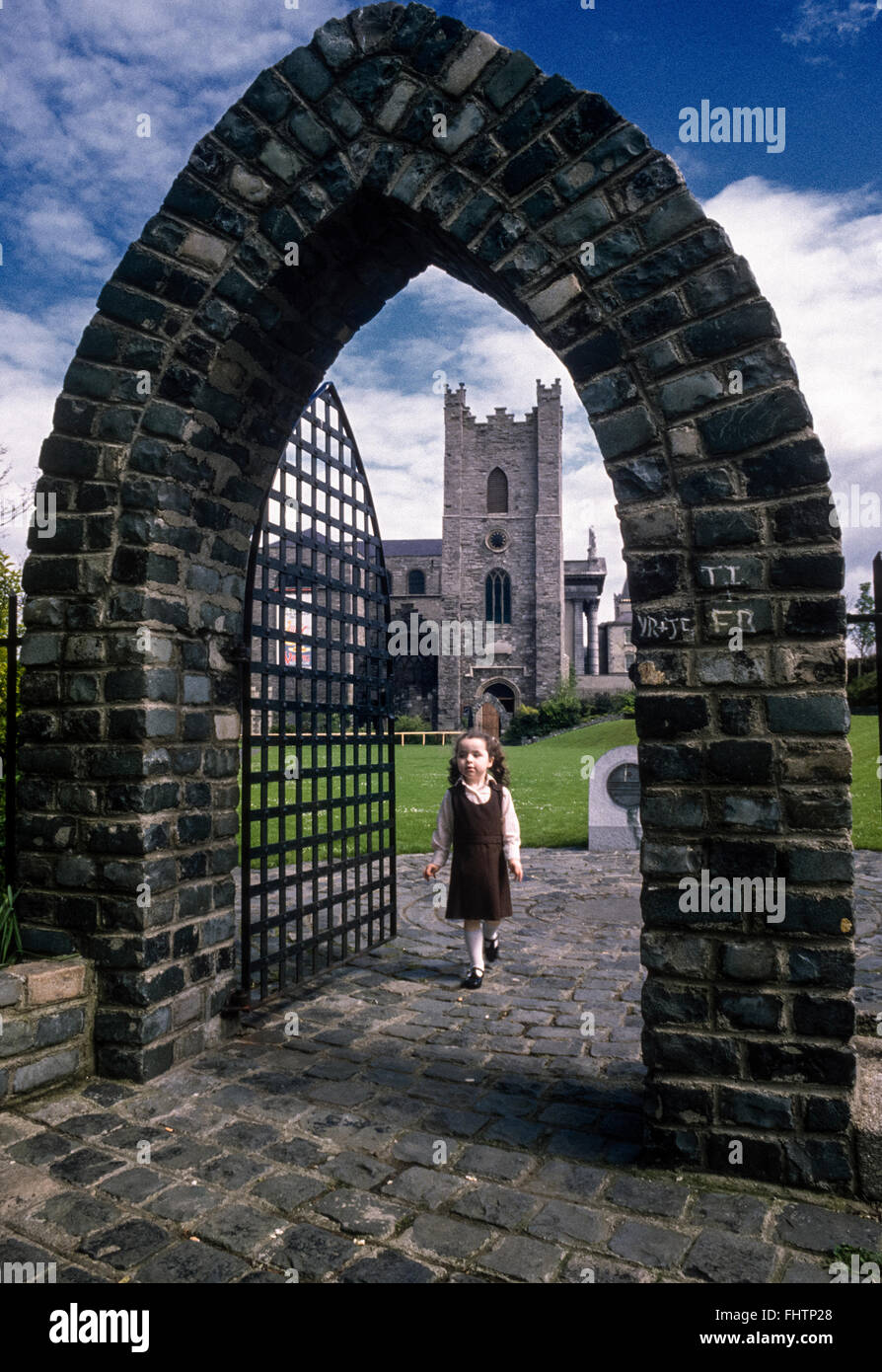 Un giovane schoolgirl in uniforme passeggiate attraverso il passaggio a volta all'ingresso laterale a St Audoens chiesa, Dublino, Irlanda, metà anni ottanta. Scansione da 35mm trasparenza. Foto Stock