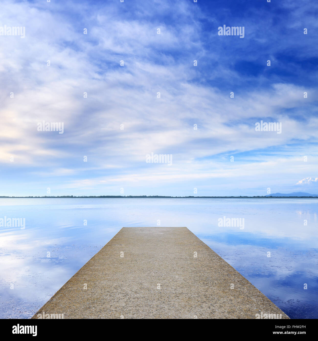 Molo di cemento o un pontile e su un lago blu e il cielo nuvoloso la riflessione sull'acqua. Foto Stock