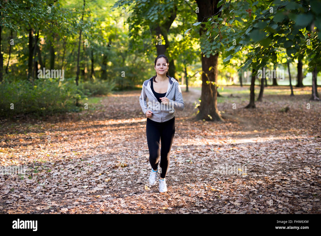 Montare la donna a fare jogging nel parco circondato da alberi verdi Foto Stock