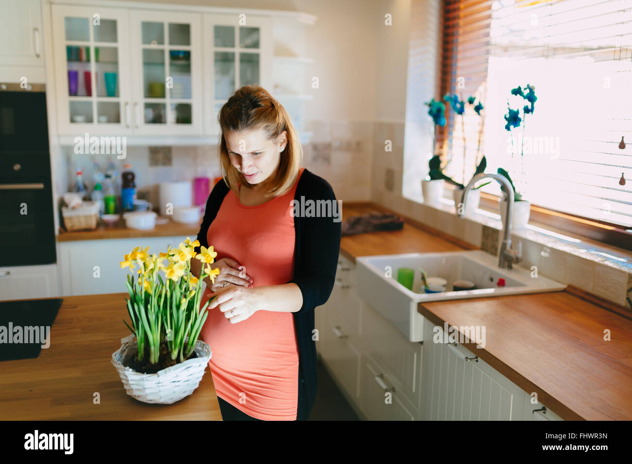 Donna incinta avendo cura di fiori in cucina moderna Foto Stock